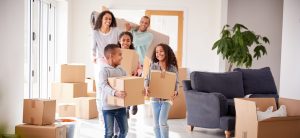A family carries boxes and home furnishings into their new home after deciding on a DIY approach to save on moving costs.